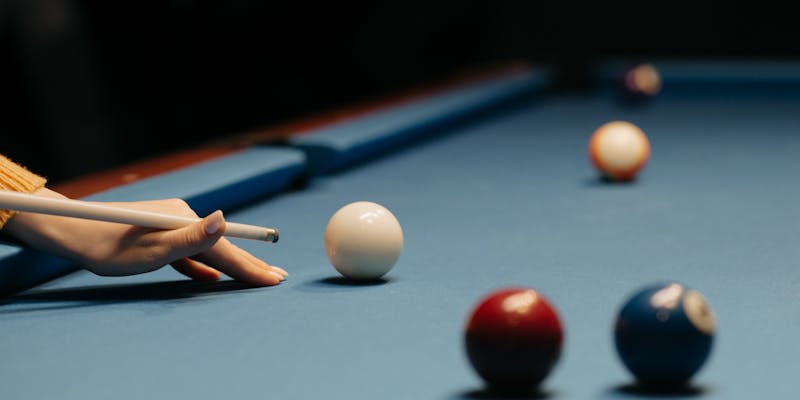 Person taking a pool shot, action view from across the billiards table