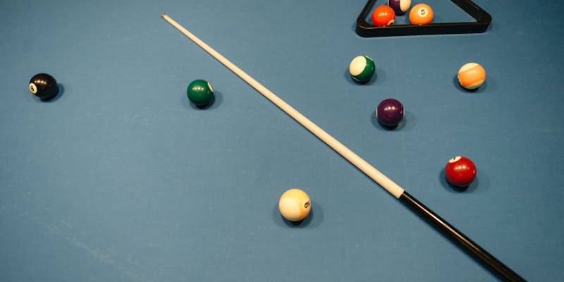 Billiard balls and cue stick on blue felt table with rack triangle