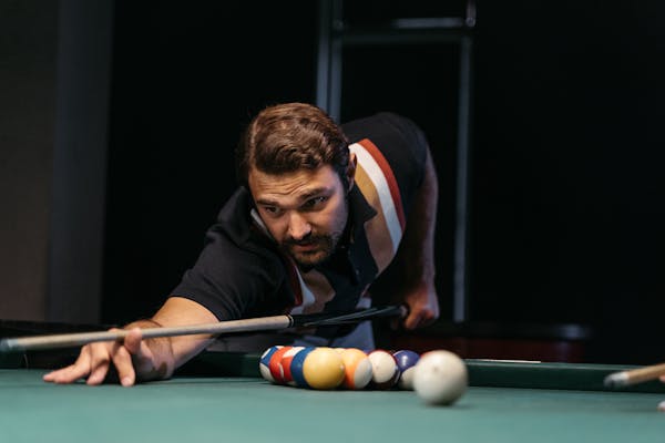Focused man lining up a shot with a cue stick at a pool table