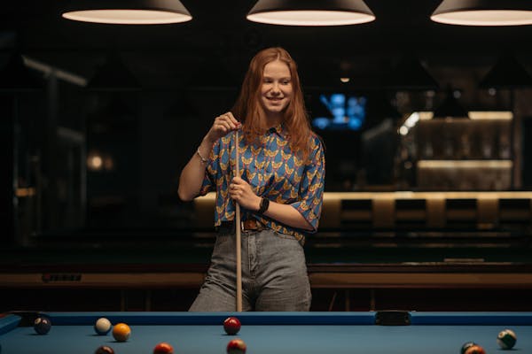 Woman holding a cue stick standing at a pool table in a billiards hall
